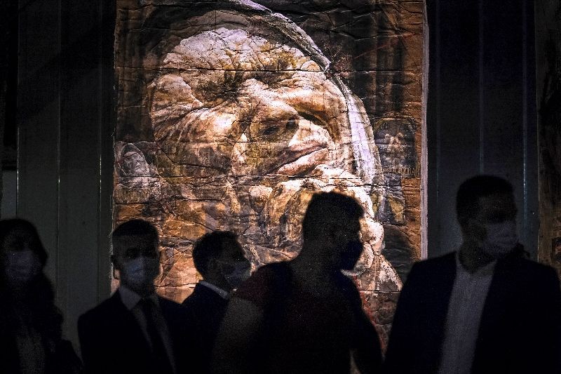 People, some wearing face masks for protection against COVID-19 infections, are silhouetted against large artworks by Bosnia's best-known living painter, Safet Zec, during the opening of his exhibition in Potocari, Bosnia. (Photo by Kemal Softic/AP Photo)